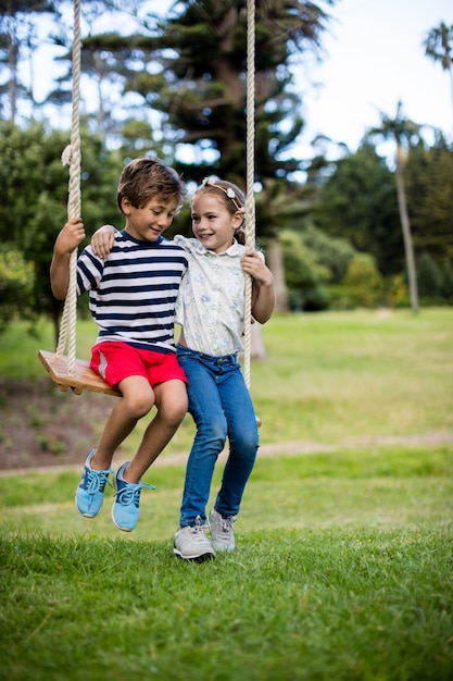 Niño y niña sentada en un columpio en el parque