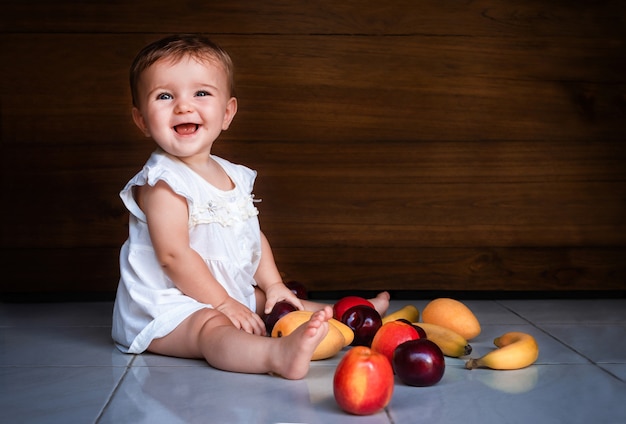 Niño niña sentada en el suelo con frutas y sonriendo sobre fondo de madera