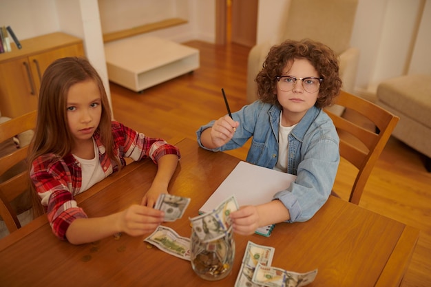 Un niño y una niña sentados en la mesa y contando dinero.