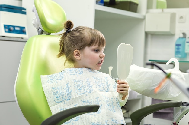 Niño niña en la silla del dentista se mira en el espejo Problema dental