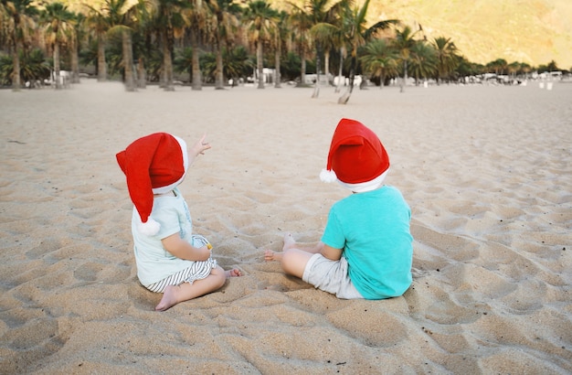 Niño y niña con sombreros rojos de santa divirtiéndose en la playa de arena del océano Niños jugando en el fondo de la costa del mar