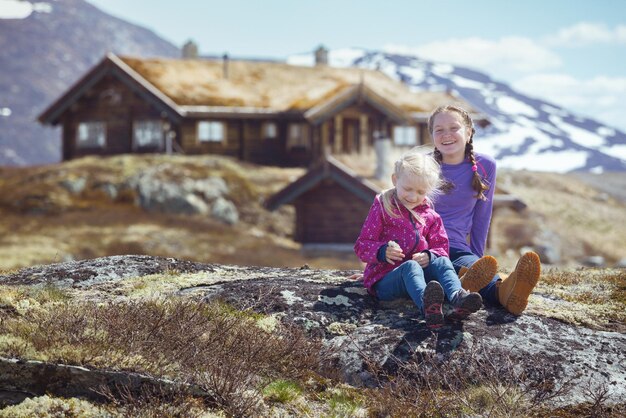 Niño niña sonriente caminante sentado sobre un fondo de antiguas casas de madera tradicionales en Tyin, Noruega