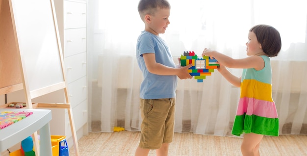 Un niño y una niña sostienen un corazón hecho de bloques de plástico Hermano y hermana se divierten jugando juntos en la habitación