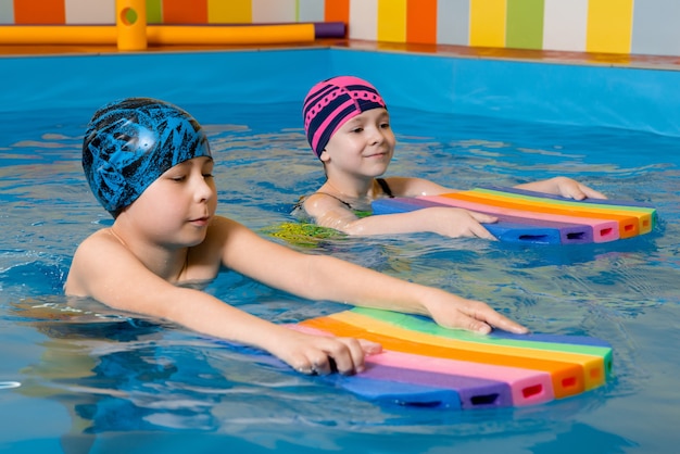 Niño y niña en traje de baño utiliza una almohadilla de espuma para practicar la natación en la piscina