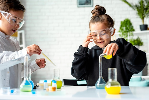 Foto niño y niña en uniforme blanco realizando experimentos químicos en el laboratorio