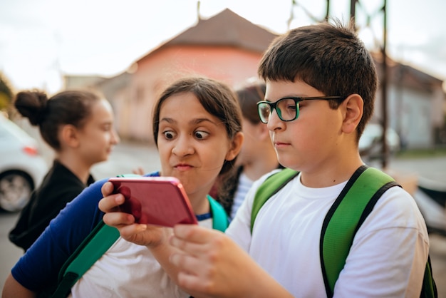 Niño y niña usando un teléfono inteligente en un camino de la escuela