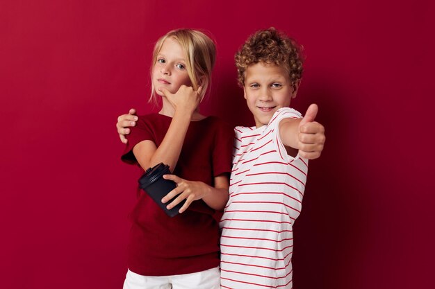 Niño y niña vaso desechable con bebida posando fondo rojo.