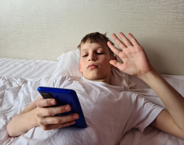 Niño niño adolescente agitando la mano en la pantalla del teléfono inteligente y hablando por videollamada