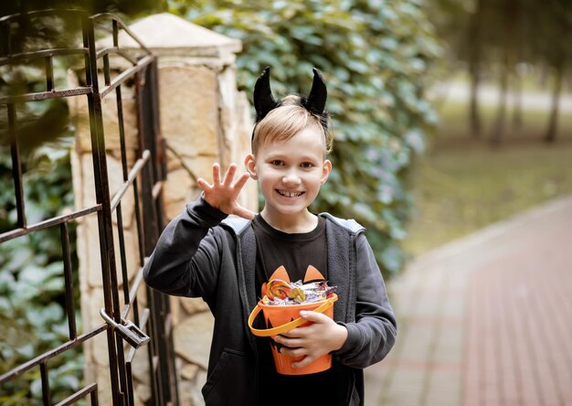 Niño niño adolescente sosteniendo un cubo de calabaza jack-o-lantern con dulces y dulces cerca de la cerca de la casa. Truco o trato para niños en las vacaciones de Halloween