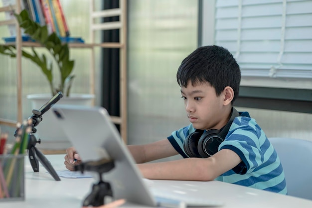 Foto niño niño en auriculares está usando una tableta y se comunica a través de internet en casa