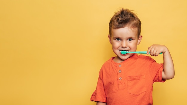 Niño niño bebé feliz cepillándose los dientes con un cepillo de dientes sobre un fondo amarillo. cuidado de la salud, higiene bucal. un lugar para tu texto.