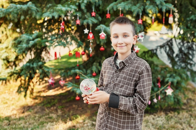 niño niño con una bola de nieve de cristal cerca del árbol de Navidad