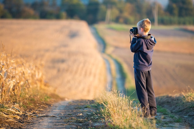 Niño niño con cámara de fotos tomando fotos del campo de trigo