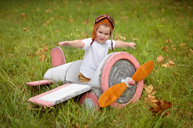 Niño niño en un casco se sienta en un avión retro y juega en la naturaleza en el verano.