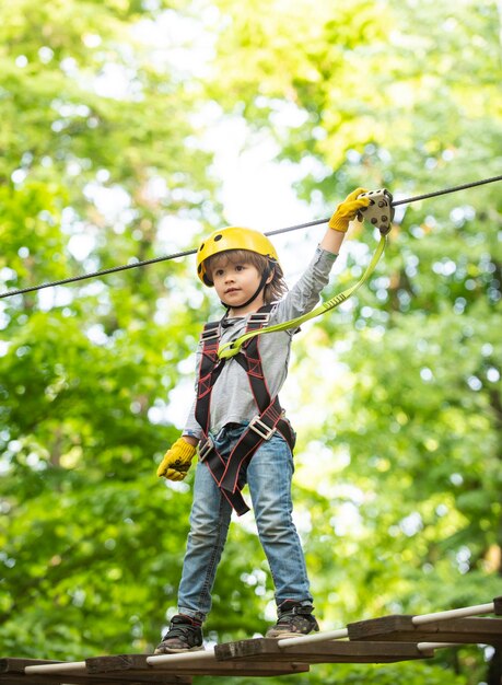 Niño niño divirtiéndose en el parque de aventuras infancia despreocupada niño escalando en el parque de cuerdas altas feliz iluminado...