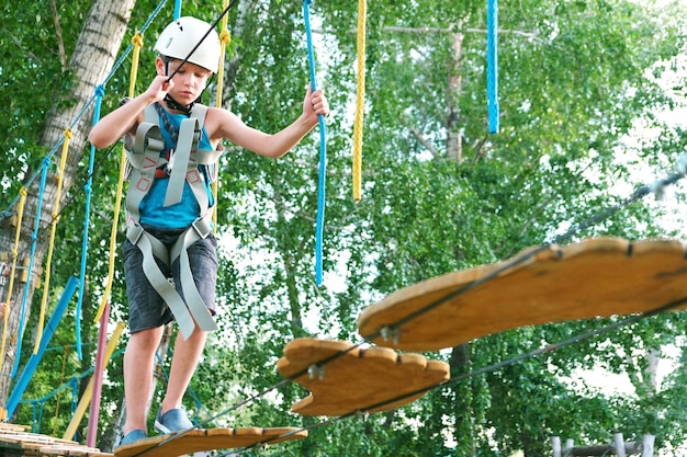 Niño niño divirtiéndose en verano en el parque de aventuras en la tirolesa. Viga de equilibrio y puentes de cuerda.