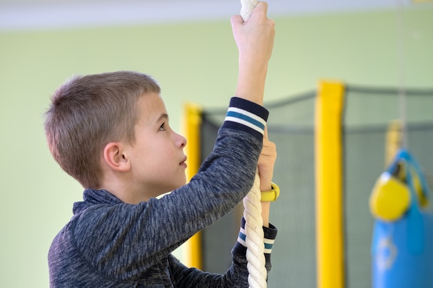 Niño niño ejercicio en una barra de escalera de pared dentro de la sala de gimnasio deportivo en una escuela.