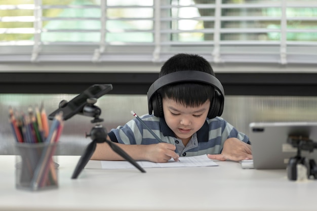 El niño niño está utilizando se comunica en Internet en casa. educación en el hogar, aprendizaje a distancia, niño asiático que toma una clase en línea y feliz por la Cuarentena de educación en el hogar.