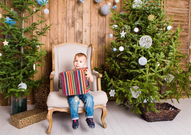 Niño niño feliz con caja de regalo cerca del árbol de Navidad.