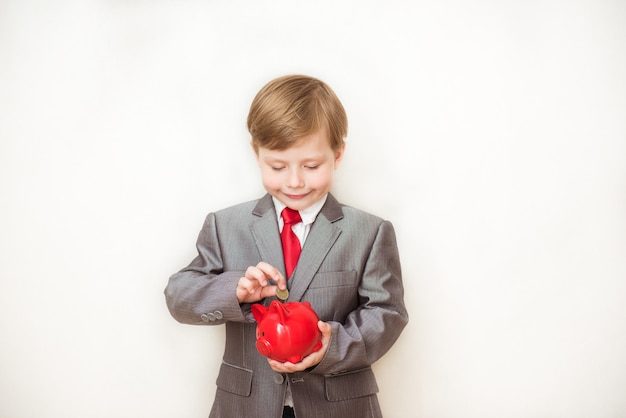 Niño niño feliz se encuentra en un traje de moda con una alcancía en sus manos. Concepto de negocio de éxito, creatividad e innovación