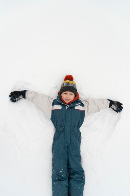 Niño niño feliz jugando en invierno en la nieve. Niño haciendo ángel de nieve. Vista superior. Marco vertical.