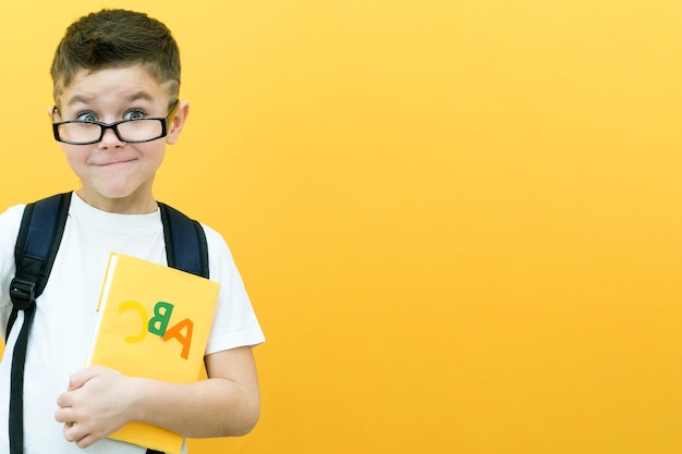 Niño niño en gafas sobre un fondo de pared amarilla Gran idea Feliz sonriente colegial vuelve a la escuela Éxito motivación ganador genio concepto libro de texto en la mano