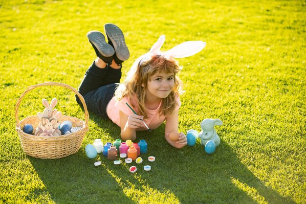 Niño niño con huevos de Pascua y orejas de conejo sobre hierba pintando huevos