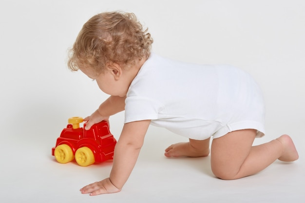 Niño niño jugando con coche de juguete, posando a cuatro patas aislado sobre blanco