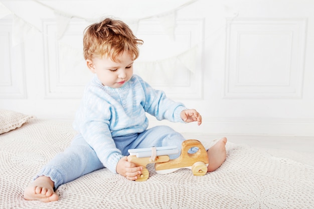 Niño niño jugando en su habitación con un coche de juguete de madera.