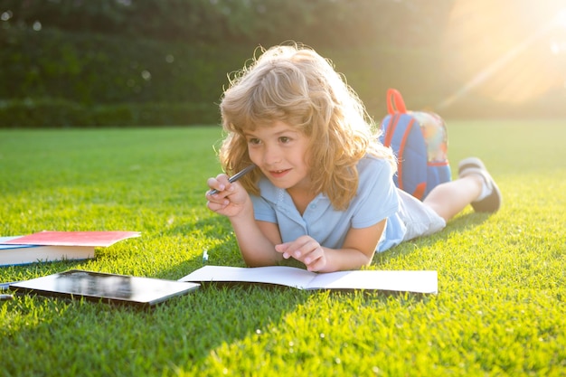 Niño niño leyendo un libro tirado en la hierba lindo niño pequeño en ropa casual con lápiz escribiendo en no