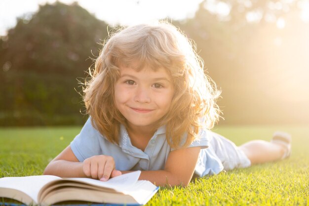 Niño niño leyendo un libro tirado en la hierba lindo niño pequeño en ropa casual leyendo un libro y sonriendo