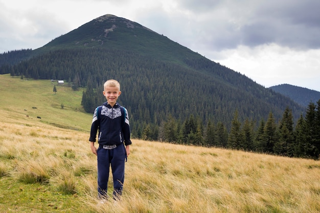 Niño niño con mochila de pie en el valle de hierba de montaña