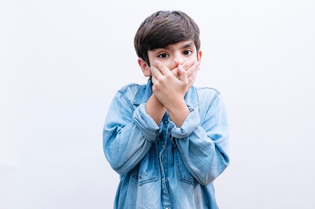 Niño niño pequeño cubre la boca con la mano sorprendido de vergüenza por error, expresión de miedo, asustado en silencio, concepto secreto