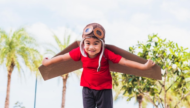 niño niño pequeño sonrisa usar sombrero de piloto y gafas jugar juguete cartón ala de avión volando