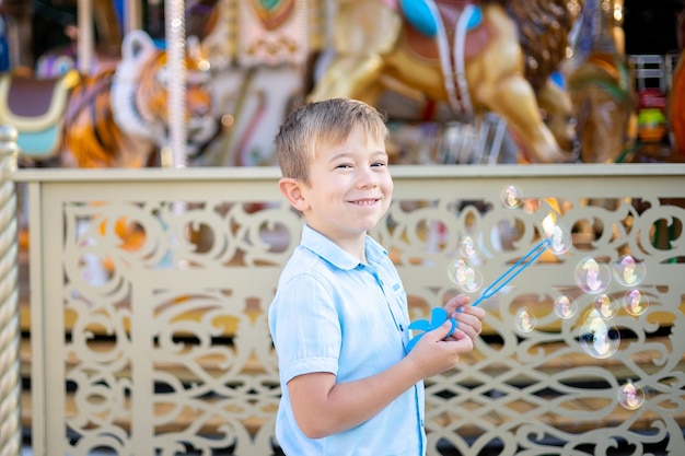 Un niño un niño rubio en un parque de atracciones infla pompas de jabón