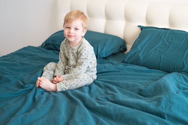 Niño niño sano en pijama verde sonriendo sentado en la cama en casa.