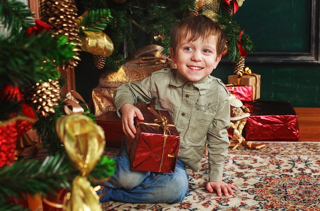 Niño niño sentado bajo el árbol de Navidad con caja de regalo.