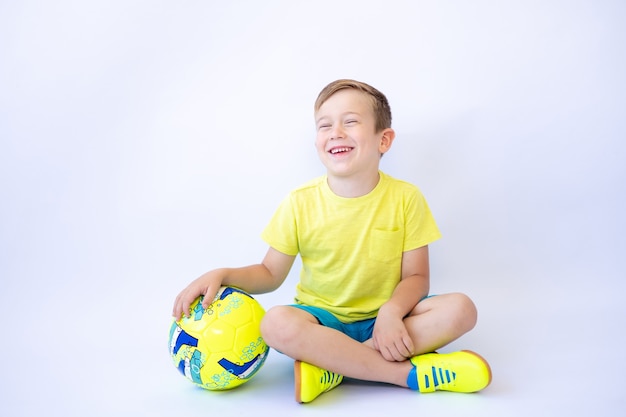 Foto un niño niño está sentado sobre un fondo blanco sosteniendo una pelota de fútbol en sus manos un estilo de vida saludable