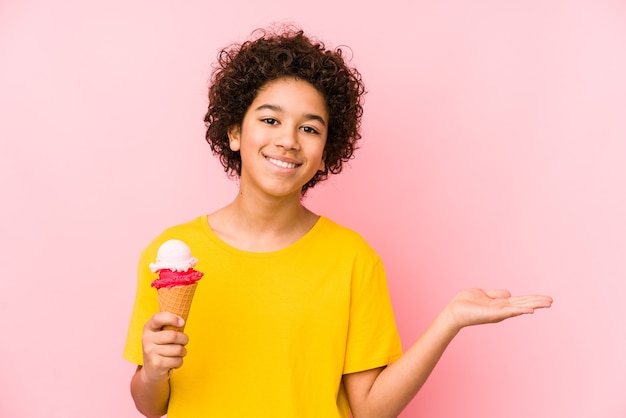 Niño niño sosteniendo un helado aislado mostrando un espacio de copia en una palma y sosteniendo otra mano en la cintura.