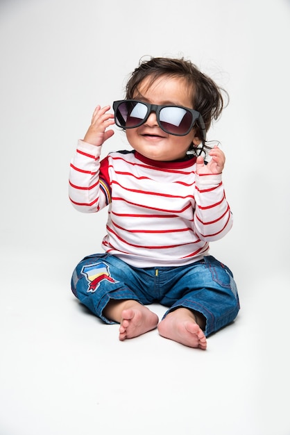 Niño o bebé indio tratando de usar gafas oscuras o gafas de sol o gafas, aislado sobre fondo blanco.