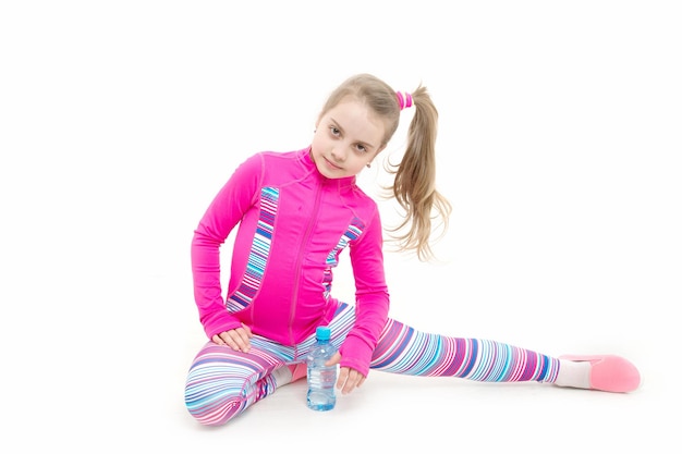 Niño o niña pequeña en ropa deportiva rosa estirando o entrenando gimnasia aislada en blanco con botella de agua, deporte y salud