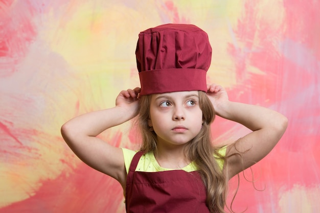 Niño o niña con sombrero de cocinero o chef y delantal en cocina de fondo abstracto colorido y moda