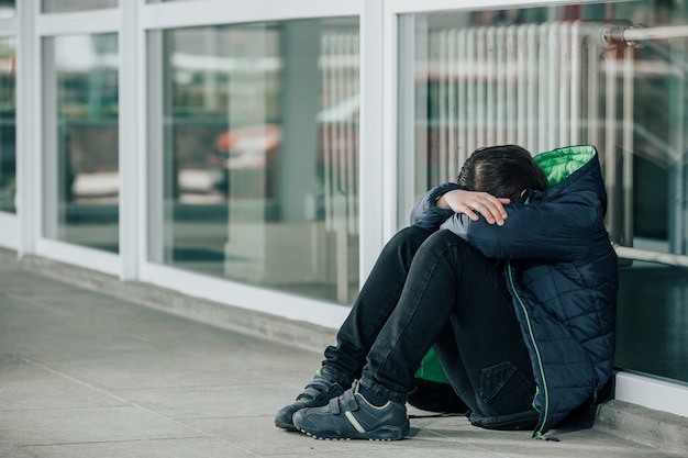 Niño o niño sentado solo en el piso frente a la escuela después de sufrir un acto de acoso escolar