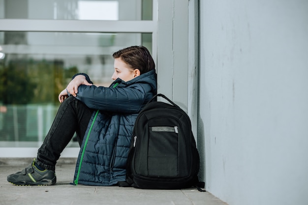 Foto niño o niño sentado solo en el piso frente a la escuela después de sufrir un acto de acoso escolar