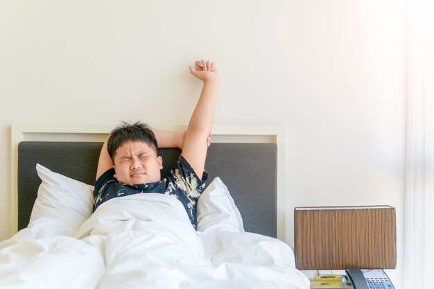 Niño obeso se despierta y estira el brazo en la cama por la mañana. concepto perezoso