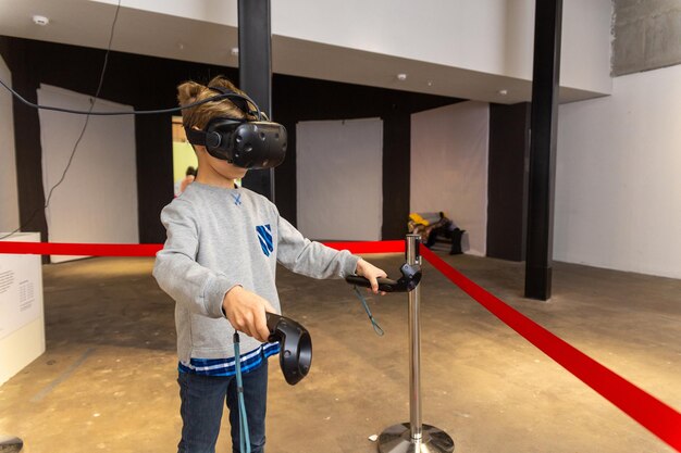 Niño de ocho años con auriculares VR sosteniendo controladores en las manos y disfrutando de una nueva experiencia en videojuegos