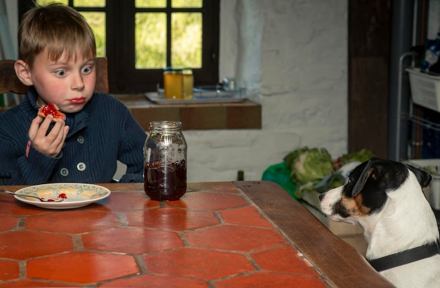 Un niño de ocho años come en una mesa con un perro.