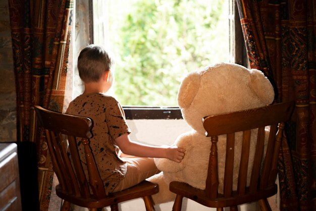 Un niño de ocho años se sienta en una ventana abierta con un oso de peluche.