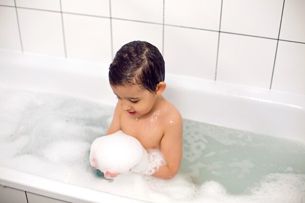 Niño de ojos grandes se baña en un baño blanco con espuma