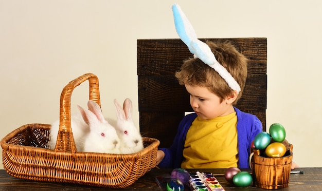 Niño con orejas de conejo el día de Pascua. Niño con canasta con huevos pintados y conejos en canasta.